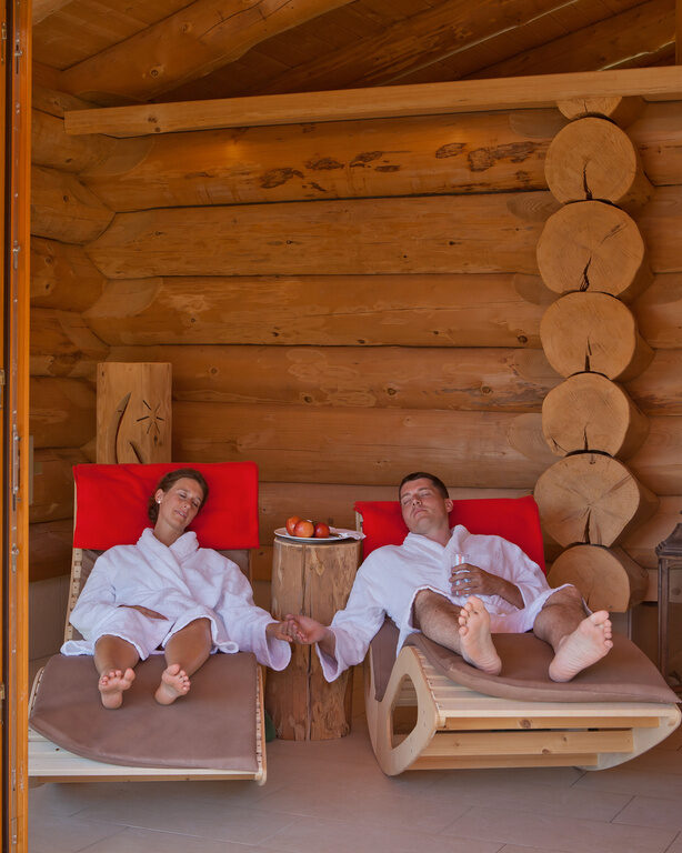 Mann und Frau entspannen auf einer Holz-Wellnessliege und halten sich an den Händen im Hotel Konradshof im Nordschwarzwald
