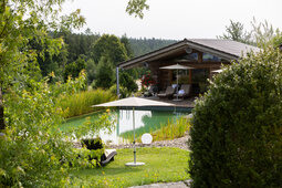 Gartenansicht über den Naturschwimmteich zu den Blockhütten vom Hotel Konradshof in Besenfeld im Nordschwarzwald