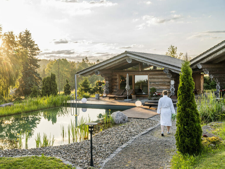 Frau im Bademantel auf dem Weg zur Blockhütte mit Sauna im Naturspa des Hotel Konradshof im Nordschwarzwald